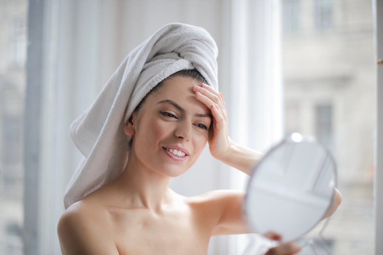 core-values A woman with a towel on her head looking in a handheld mirror and smiling.
