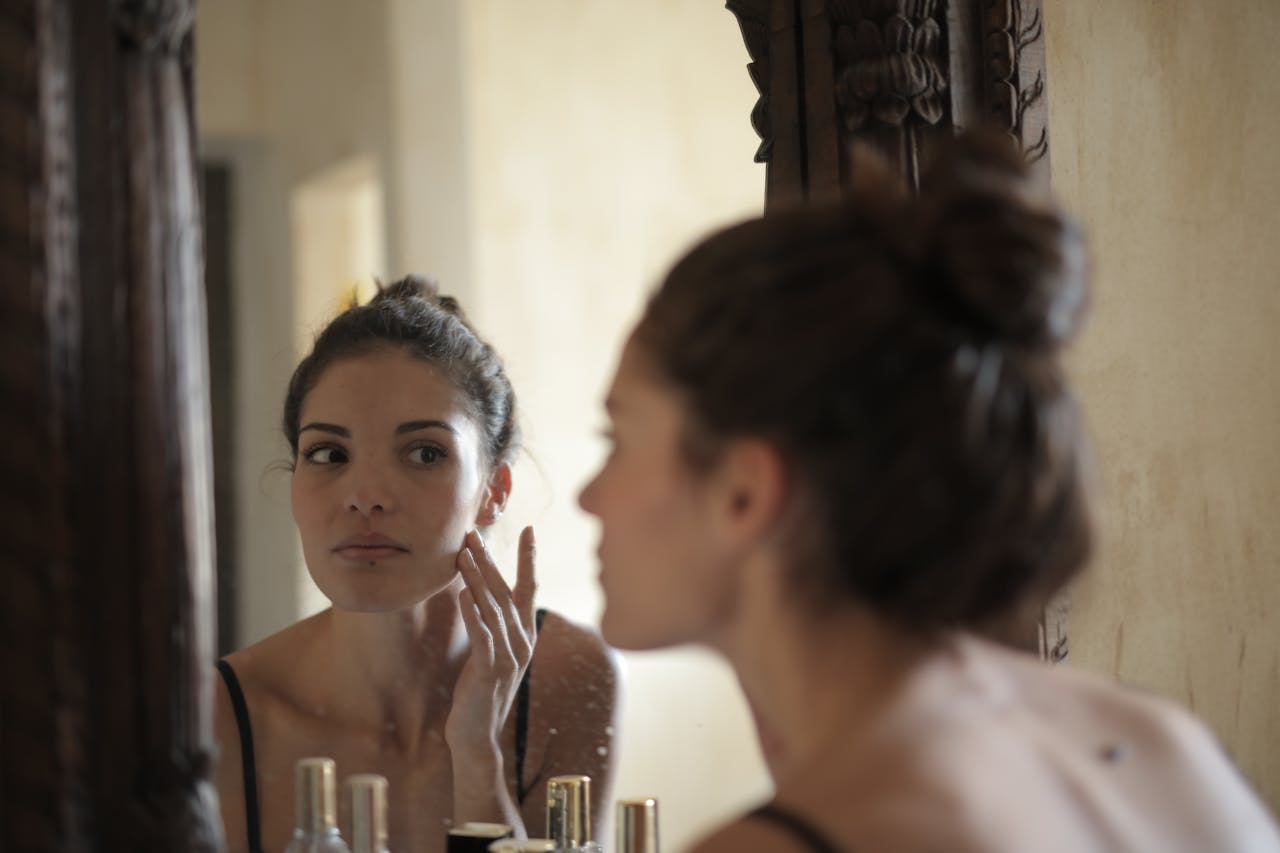 creative-approach-img A woman checks her skin in the mirror, engaging in her morning skincare routine indoors.