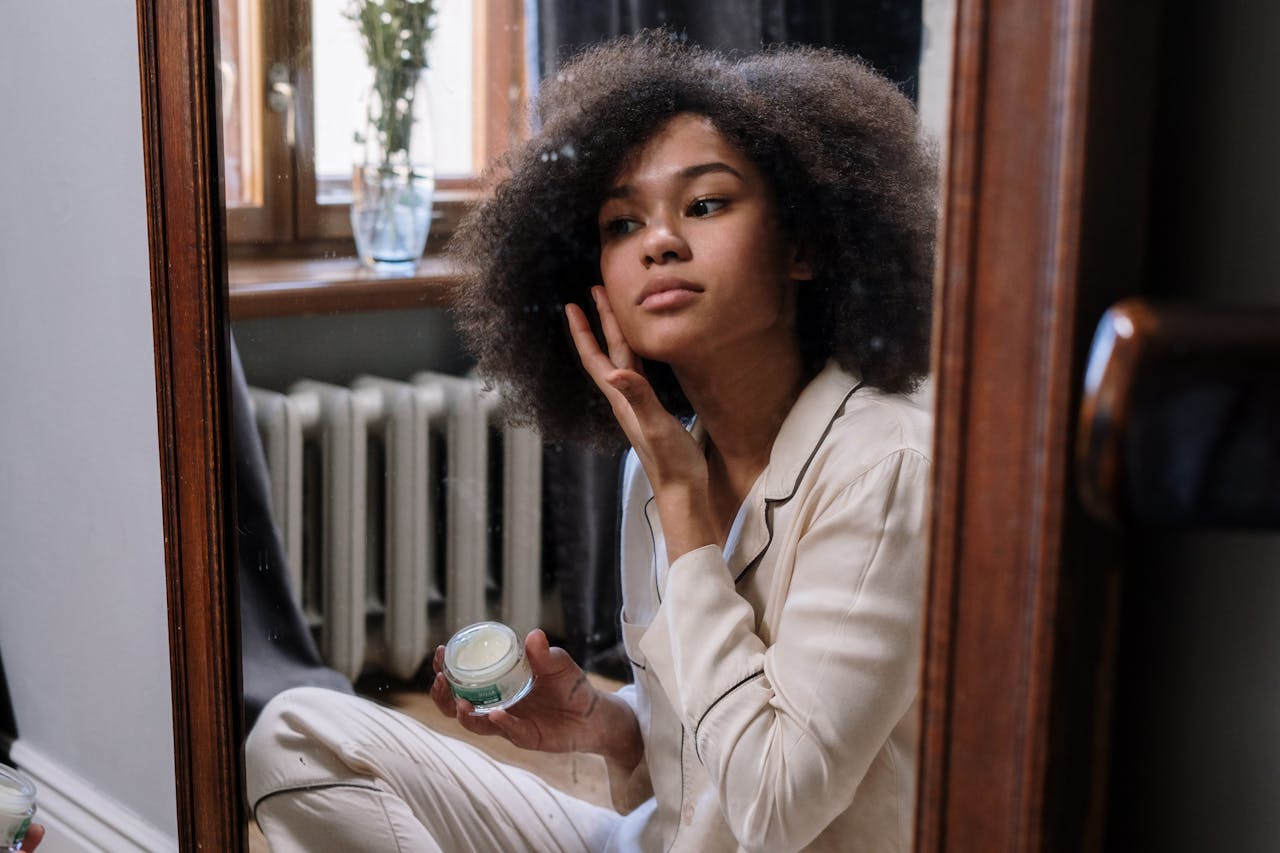 about-img A woman applies skincare cream in a cozy home environment during her morning routine.